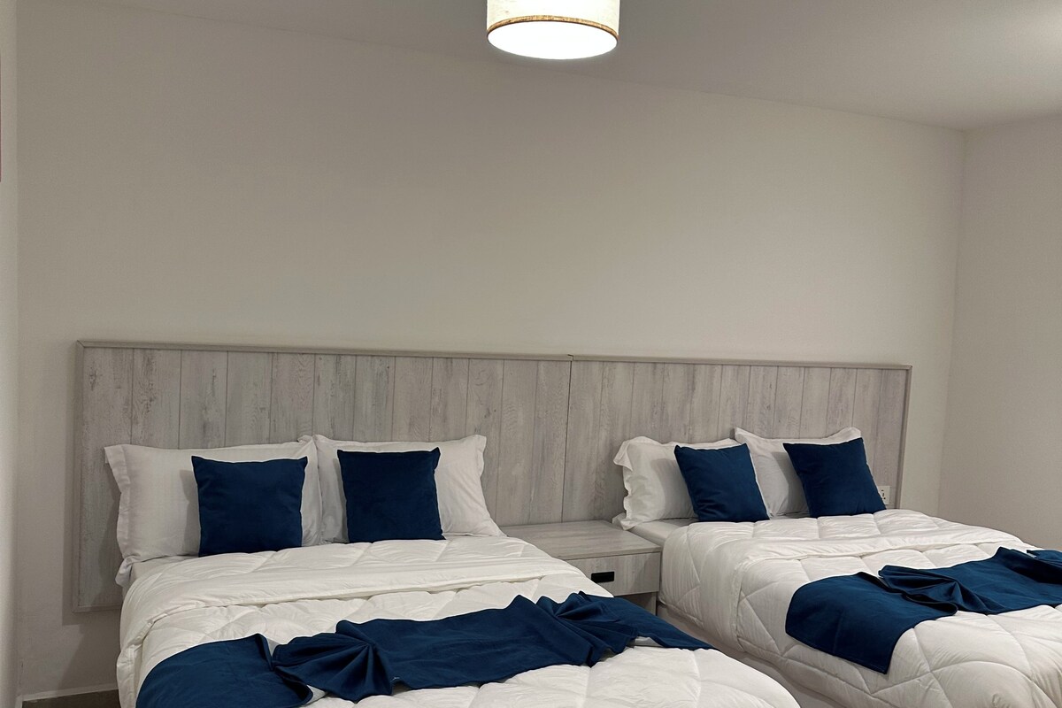 Ein Hotelzimmer mit zwei Betten, einem Holzkopfteil und einer Hängelampe.