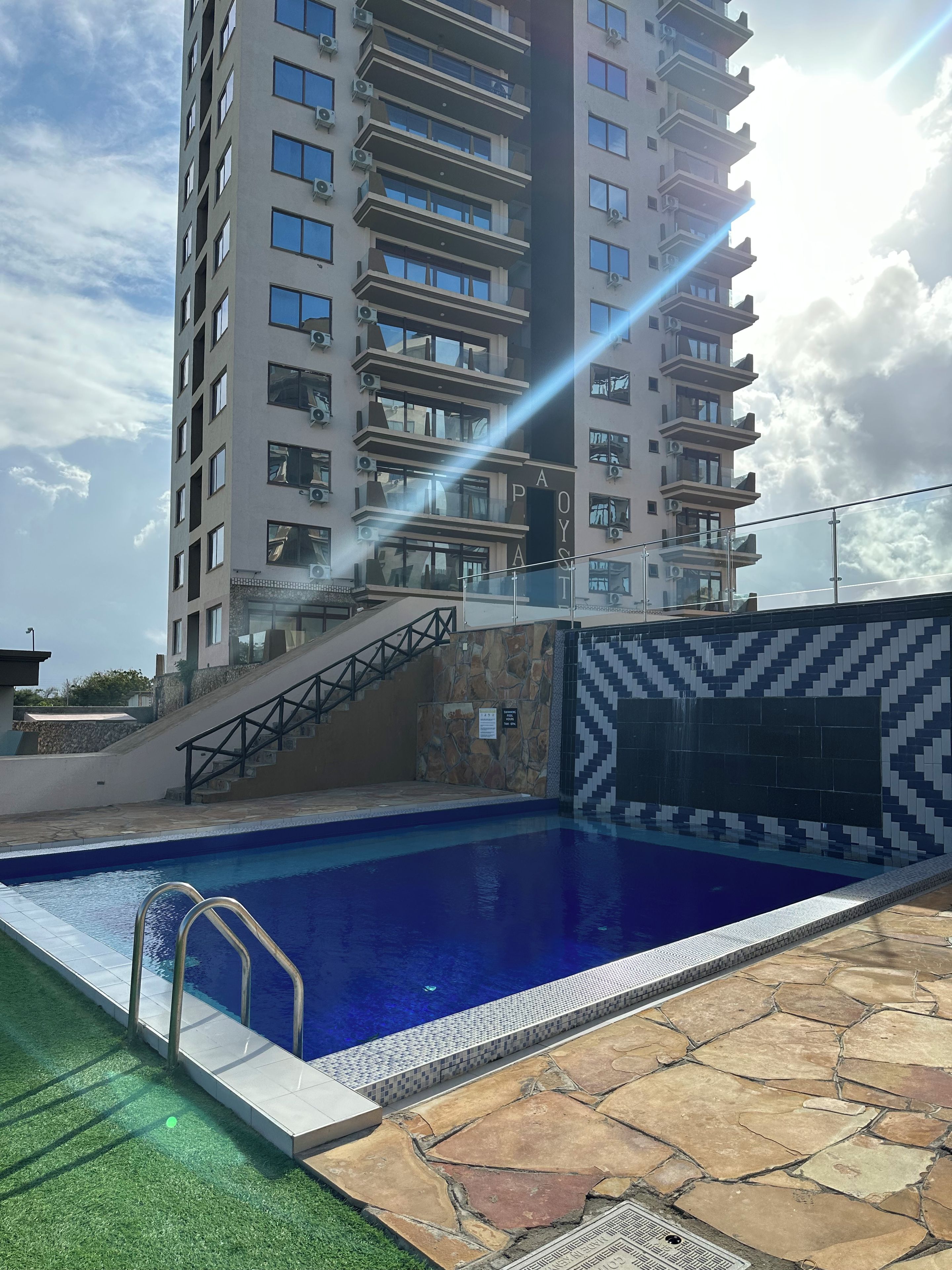 Una piscina con borde de piedra, una escalera que lleva a un edificio y un cielo despejado.