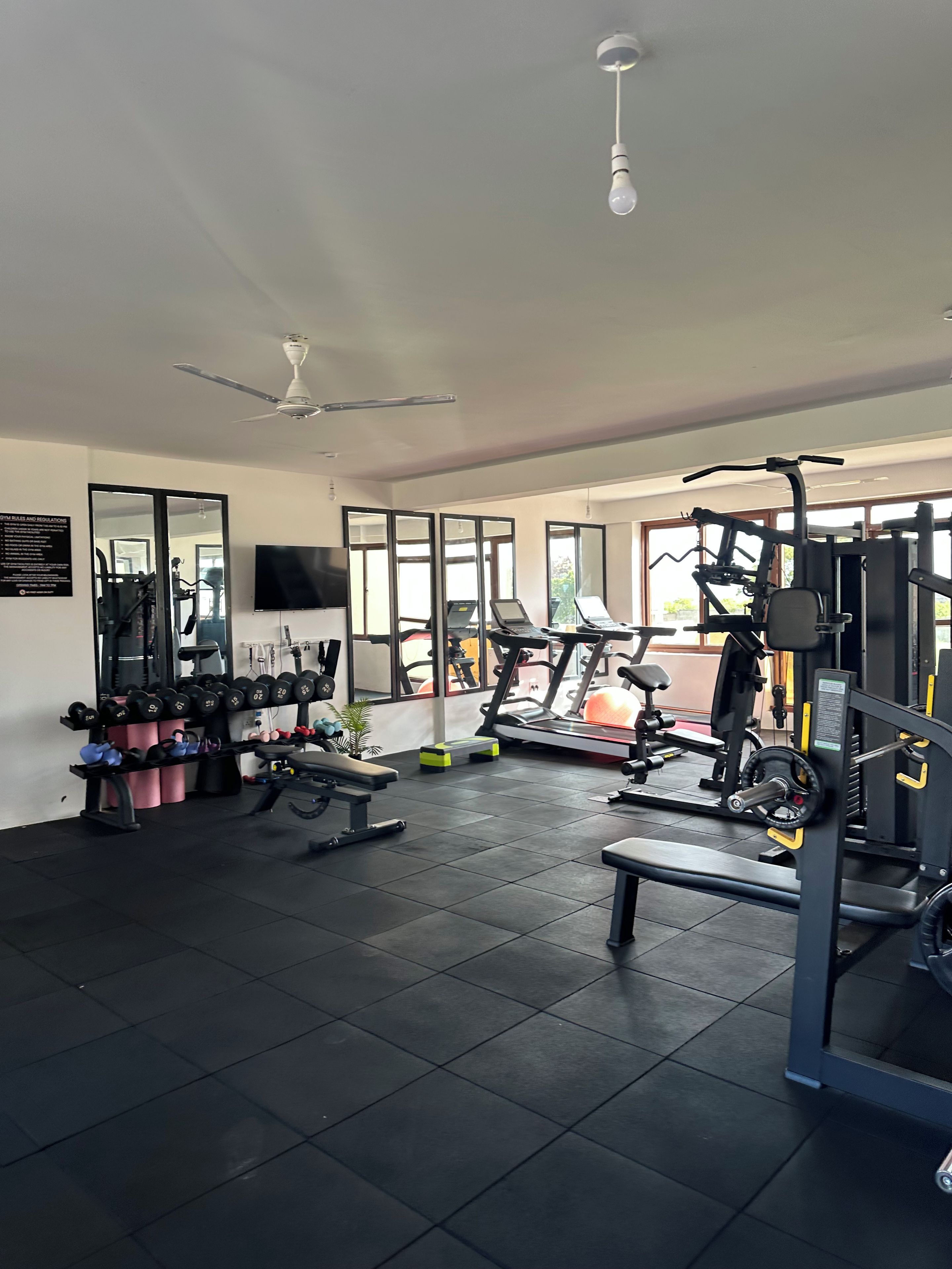 Un gimnasio con equipo de ejercicio, un ventilador de techo y ventanas amplias.
