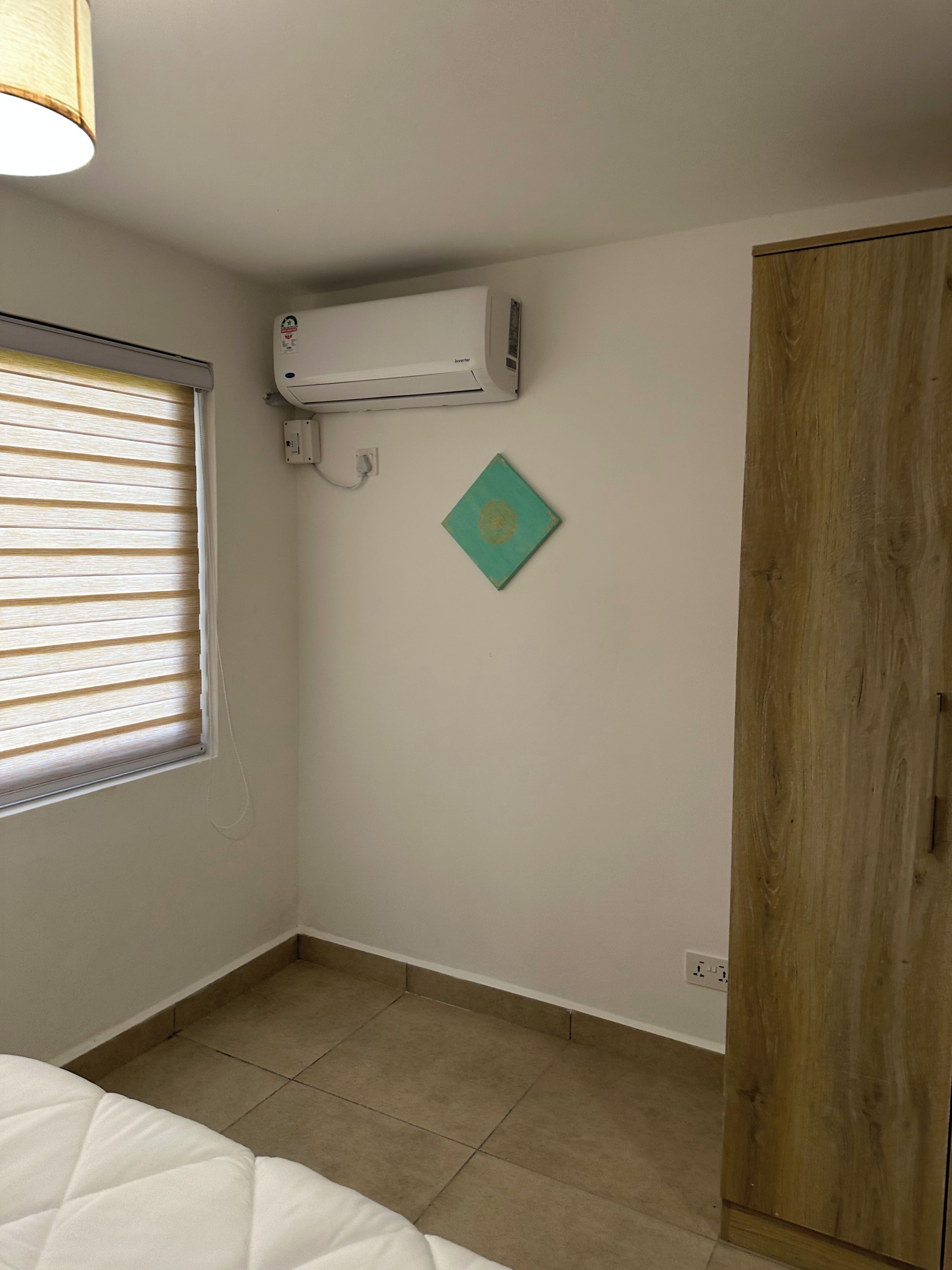 Una habitación con cama, aire acondicionado, armario de madera y ventana con persianas.