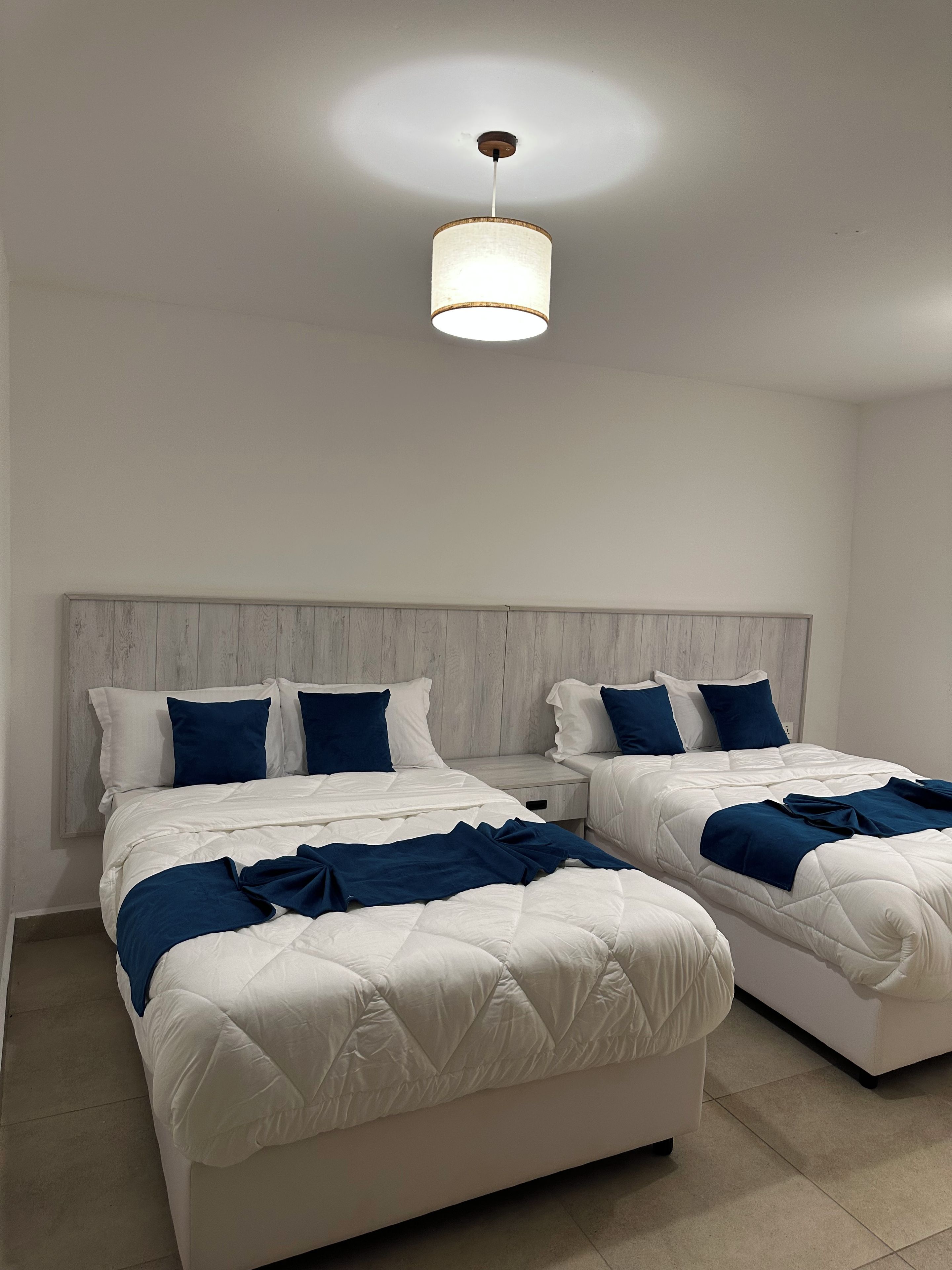 Quarto com duas camas, cabeceira de madeira e luminária no teto.