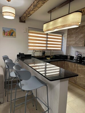 Una cucina moderna con isola centrale, sgabelli da bar, un quadro e una finestra con persiane.