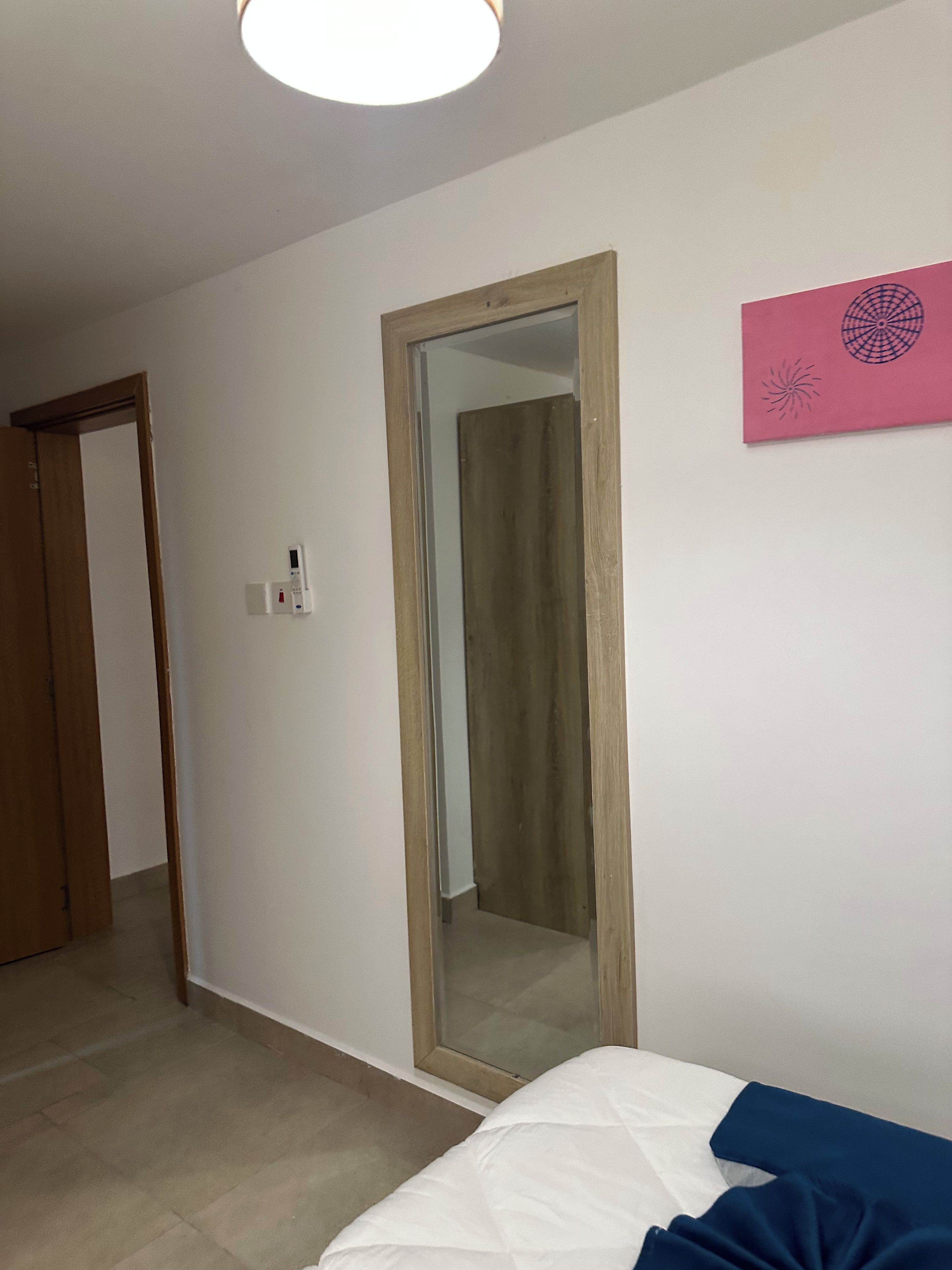 Een slaapkamer met een bed, een houten deur, een spiegel en een wandlamp.