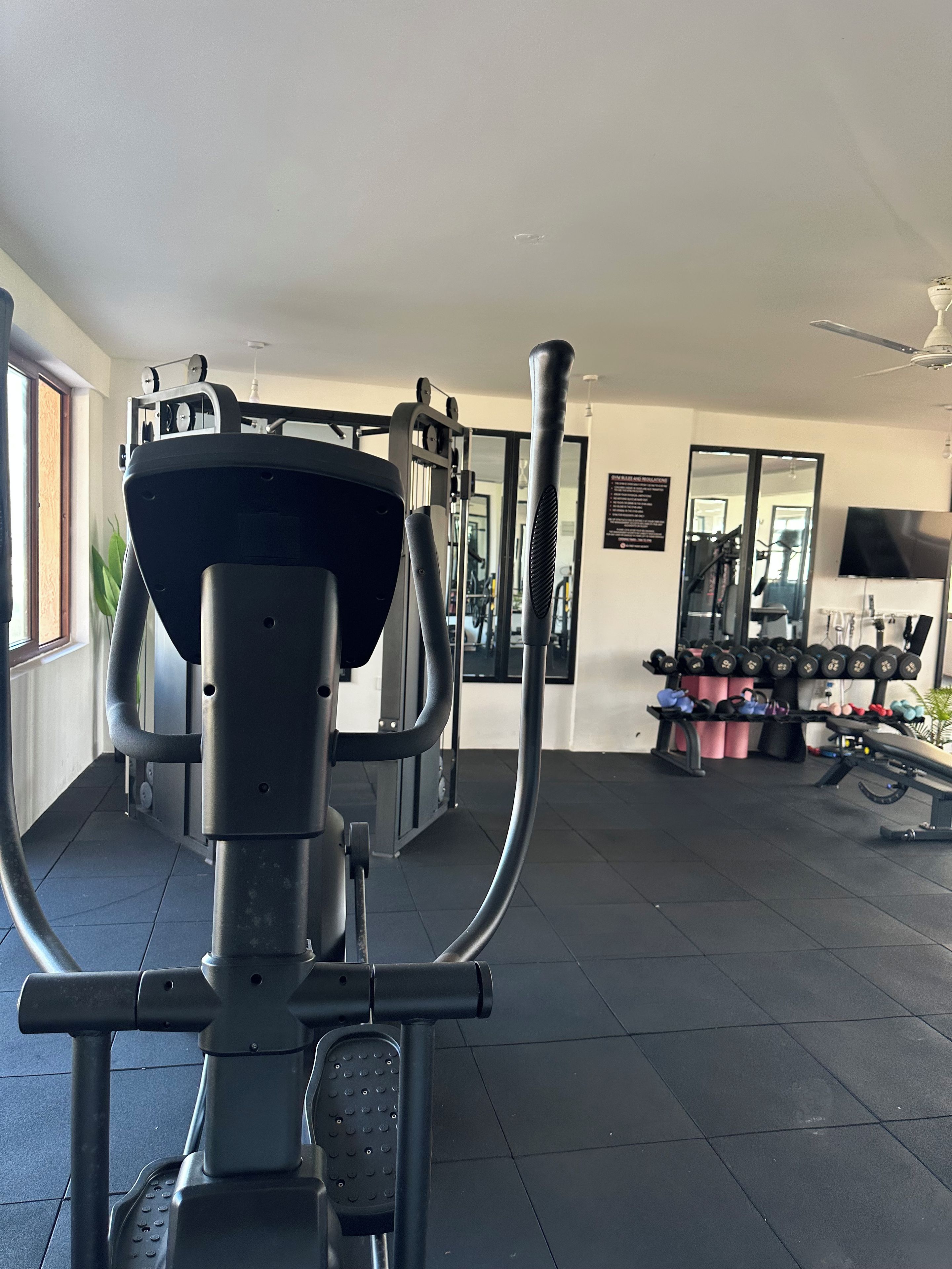 A gym with exercise equipment, a mirror, and a television on the wall.