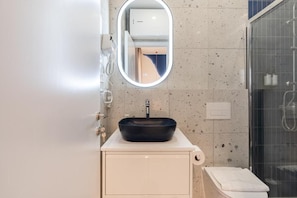 Ein Badezimmer mit rundem Spiegel, Waschbecken in Schwarz, Toilette und Duschbereich.