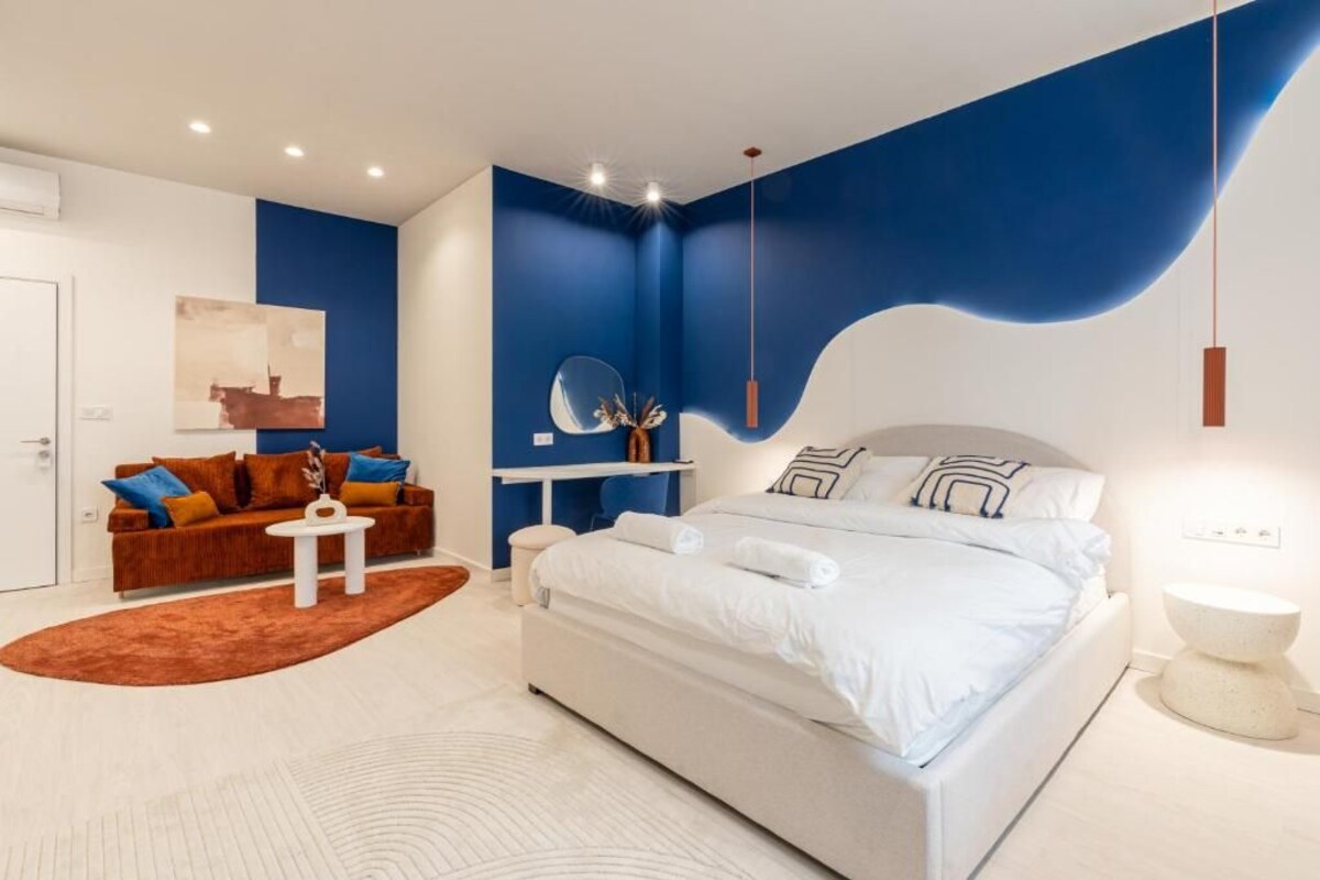 Ein modernes Schlafzimmer mit einem großen Bett, einer Couch, einem kleinen Tisch und einem Spiegel.