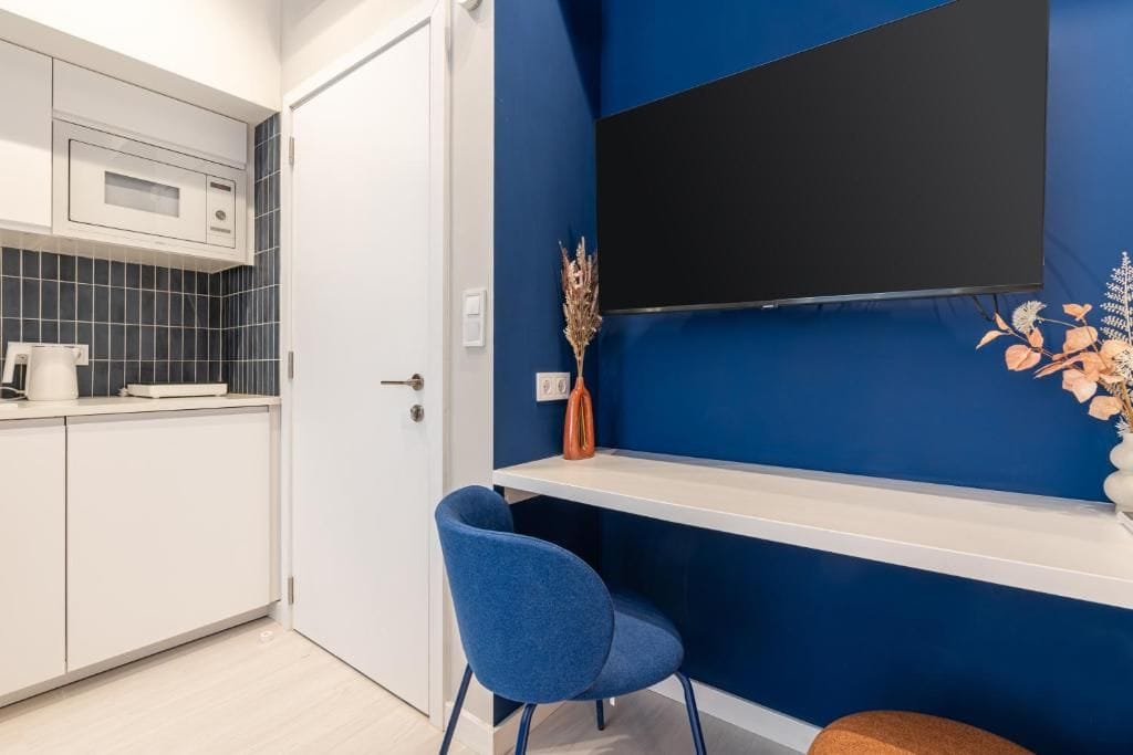 Eine moderne Küche mit weißer Arbeitsplatte, einem blauen Stuhl und einem flachbildfernseher, der an einer blauen Wand montiert ist.