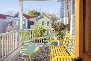 A porch with a green and yellow bench, a small table, and potted plants. - Silver Spring | The Crown Jewel Suite (Charleston)