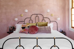 A bed with a metal frame, multiple pillows, and bedside lamps. - Silver Spring | The Crown Jewel Suite (Charleston)