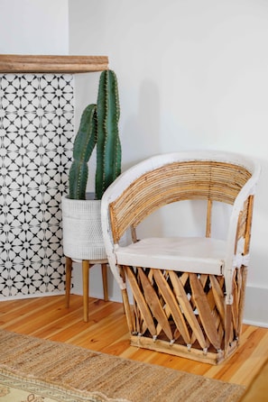 A wicker chair with a white cushion, a woven basket, and a cactus plant against a patterned wall. - Silver Spring | The Verdana Suite (Charleston)