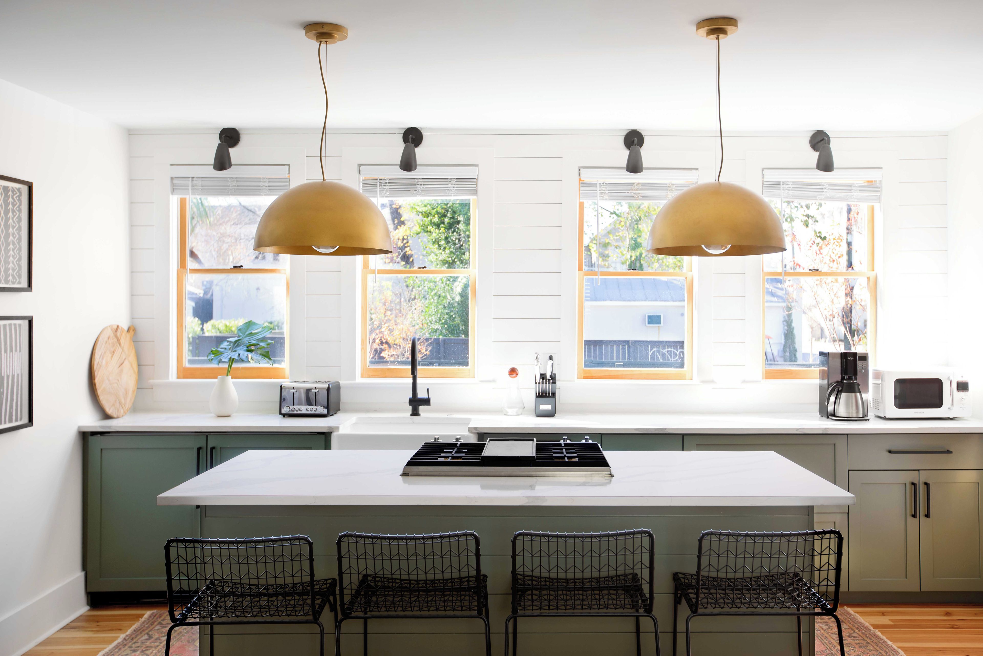 Cocina moderna con una isla central, iluminación colgante y vistas al exterior a través de amplios ventanales.