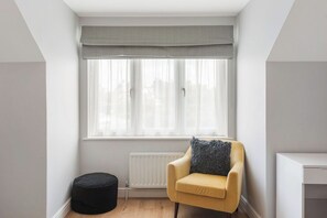 A corner room with a window, a radiator, a yellow armchair, and a black ottoman. - Charming 2-bedroom apartment in New Barnet perfect for relaxing stays (New Barnet)