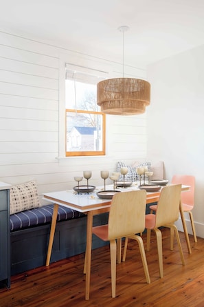 A dining area with a wooden table, four chairs, a woven pendant light, and a view of the outdoors through a window. - The Silver Spring - Prime Downtown Location (Charleston)