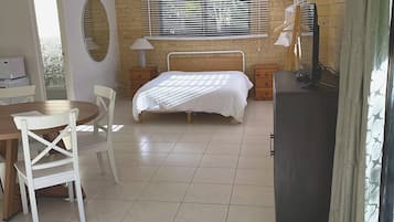 A bedroom with a bed, a desk, a chair, a mirror, and a window with blinds.