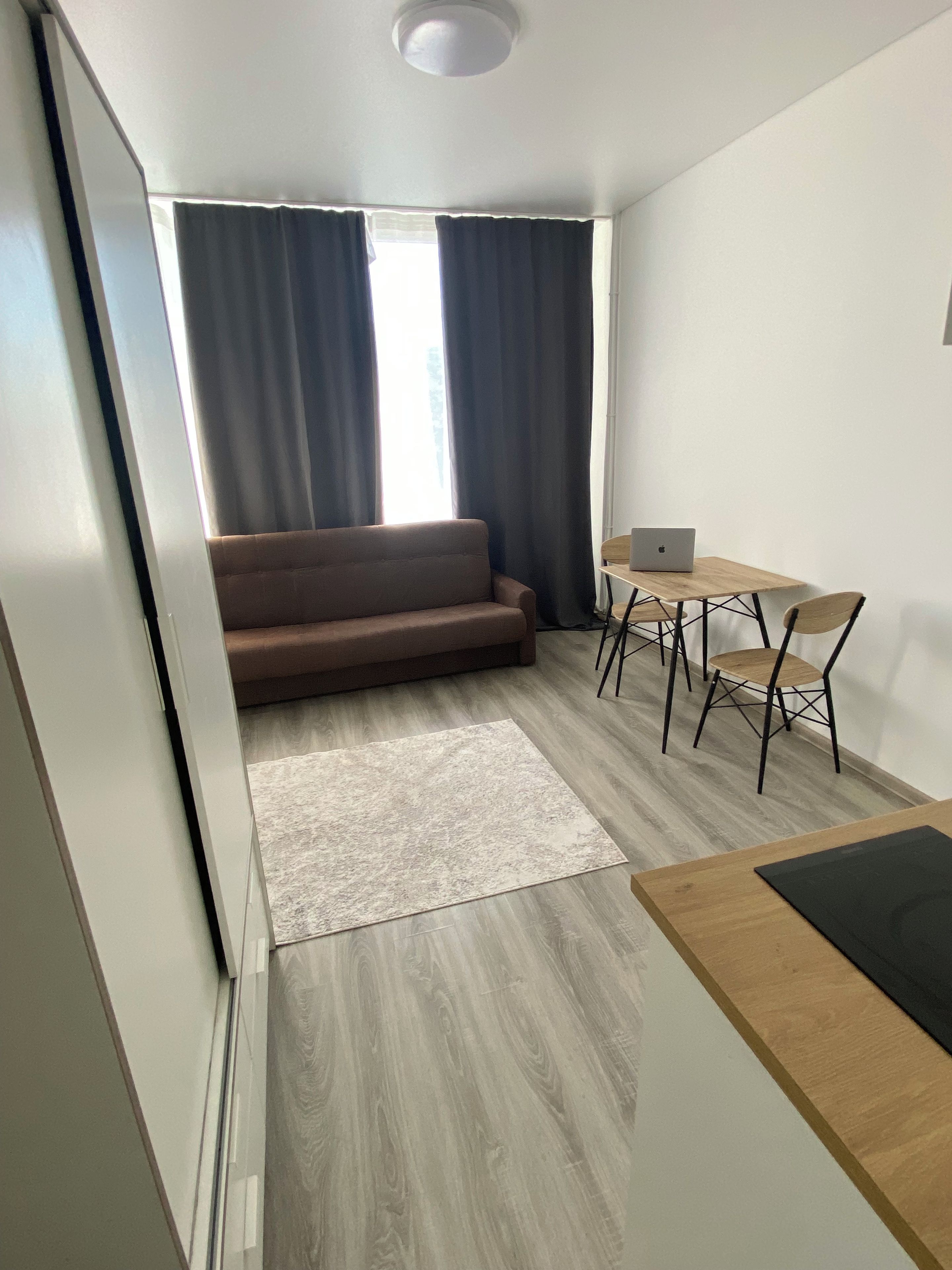 Un espacio habitable moderno con un sofá, una mesa de comedor con sillas y un ordenador portátil sobre la mesa.