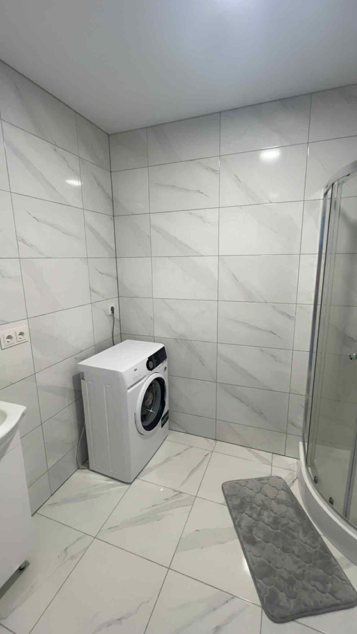 Een compacte, afgesloten badkamer met een wasmachine, douche en toilet.