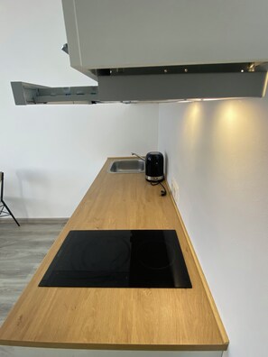 Een keuken met een houten aanrecht, een zwarte inductiekookplaat, een waterkoker en een spoelbak.