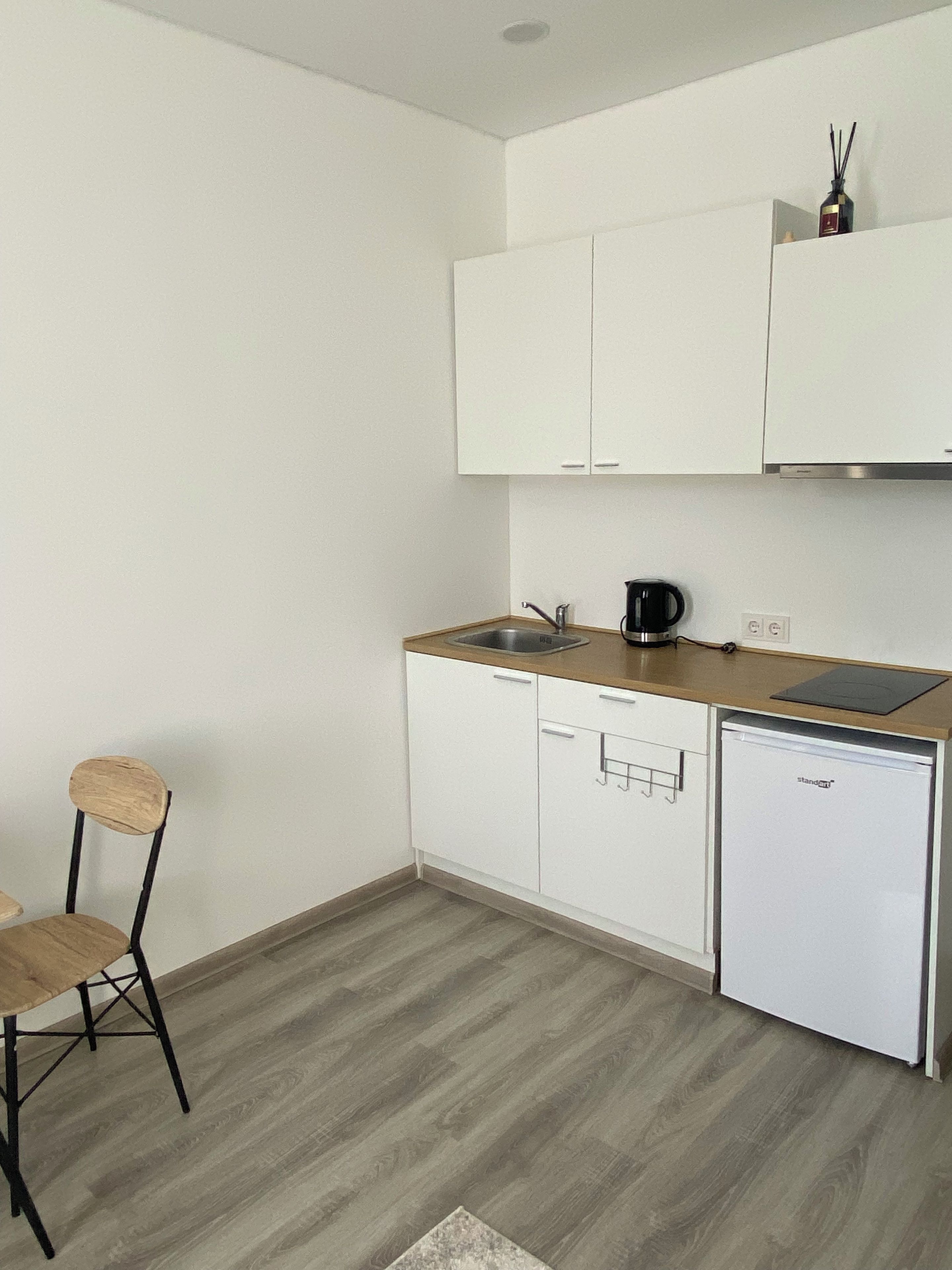 Una cocina compacta con armarios blancos, una encimera de madera, una cafetera y un refrigerador pequeño.