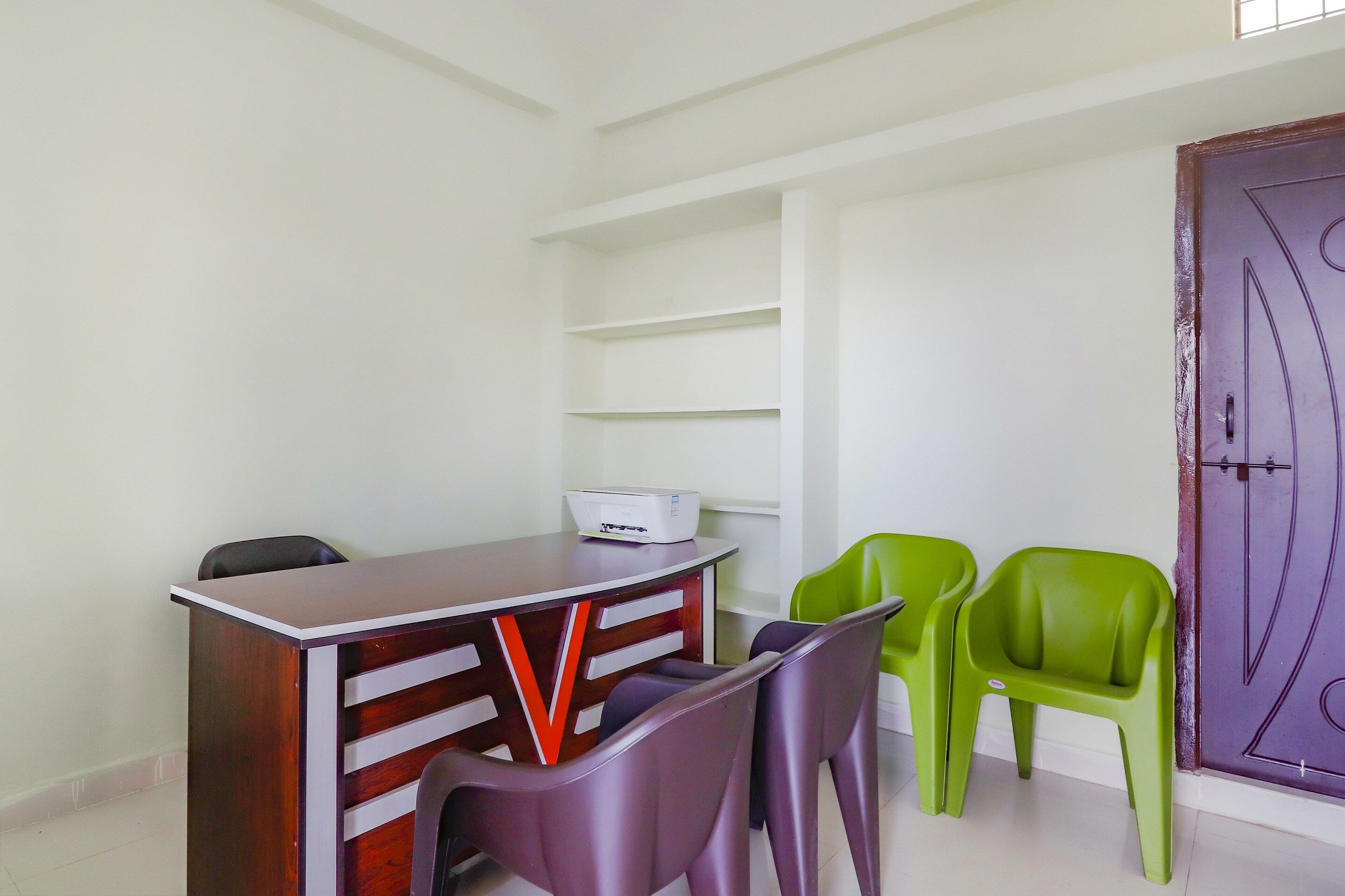 Una habitación con un escritorio de madera, dos sillas, una impresora y una puerta morada.