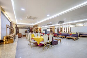 A spacious dining area with round tables and chairs, a seating area with sofas, and a chandelier. - Treebo Parth Paradise (Ghaziabad)