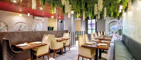A restaurant interior with multiple dining tables and chairs, a green cushioned bench, and a wall with a textured pattern.