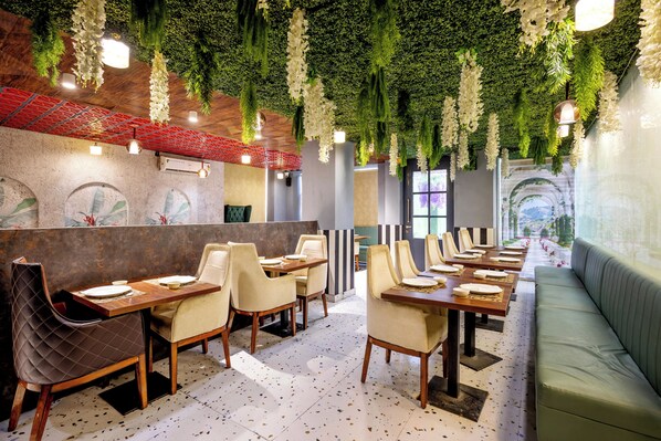 A restaurant interior with multiple dining tables and chairs, a green cushioned bench, and a wall with a textured pattern. - Treebo Parth Paradise (Ghaziabad)