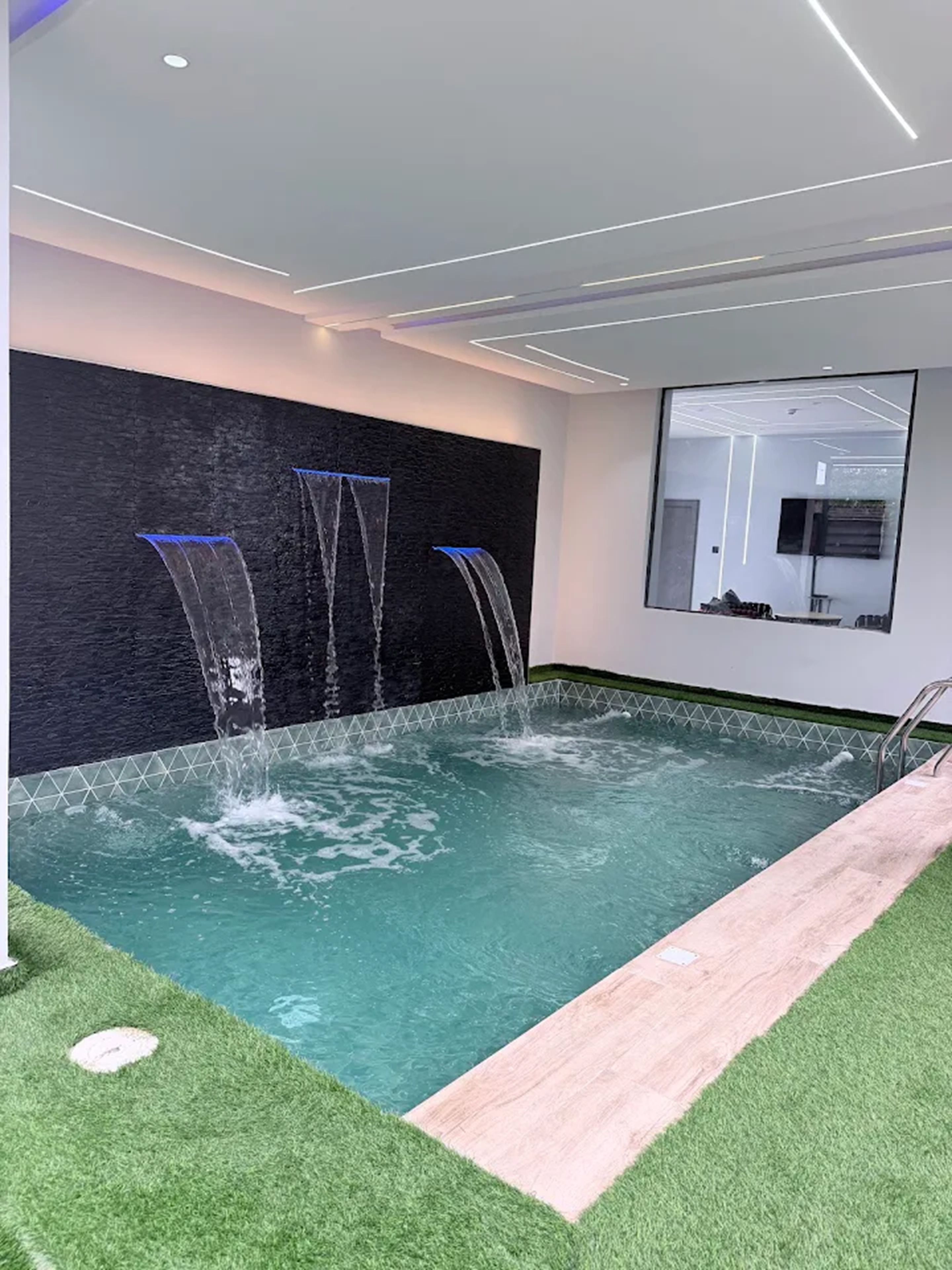 Una piscina interior moderna con pared de cristal y solárium de madera.