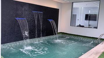 Una piscina interior moderna con pared de cristal y solárium de madera.