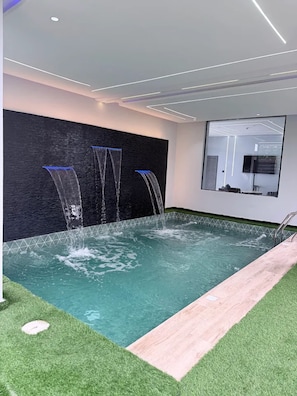 Una piscina interior moderna con pared de cristal y solárium de madera.