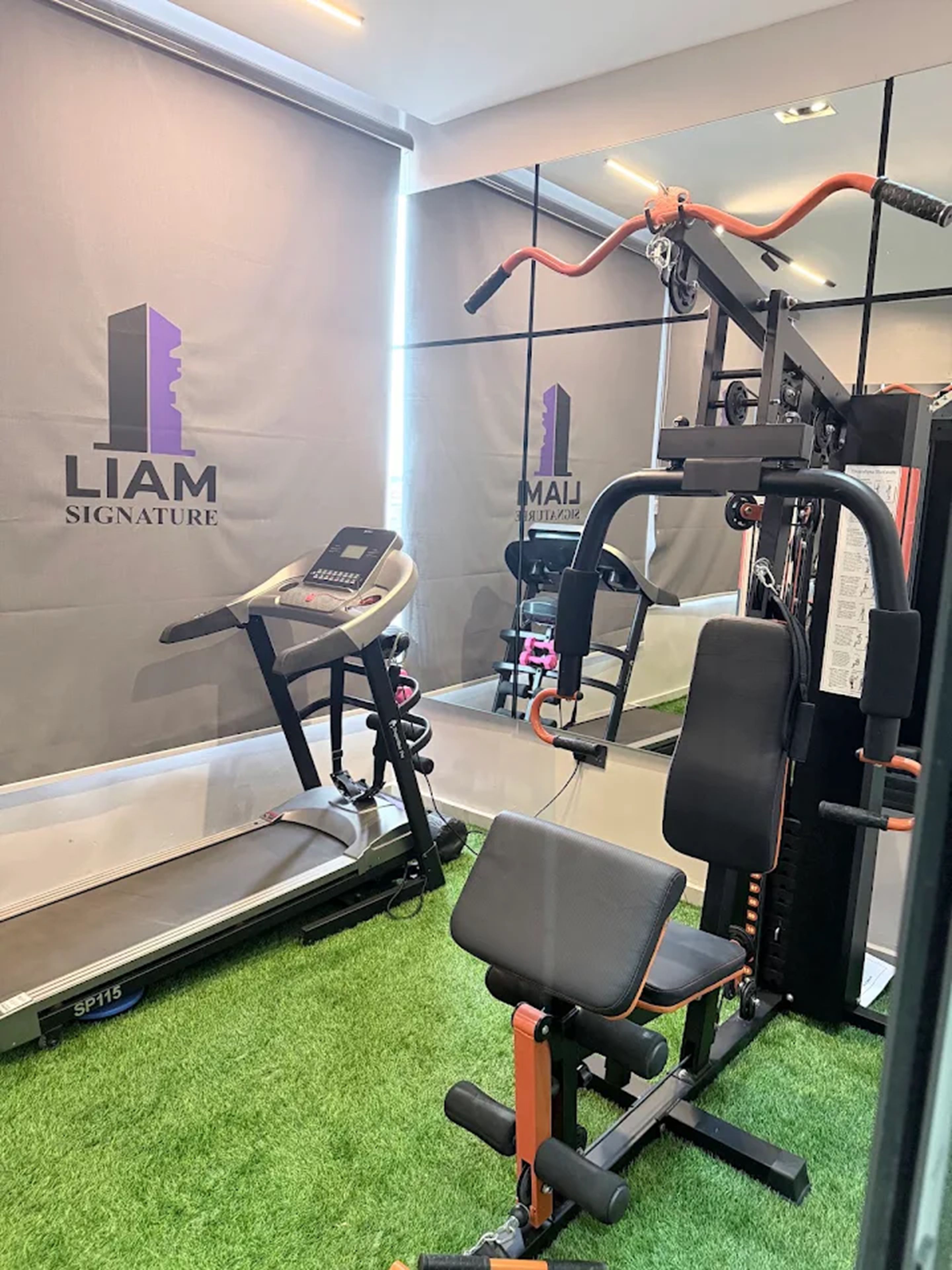 A gym with exercise equipment, a treadmill, and a wall with 'LIAM SIGNATURE' branding.