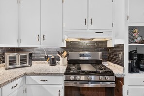 A kitchen with white cabinets, a black tiled backsplash, a stainless steel stove, and a coffee maker. - Walk to Jack Daniel Distillery & Lynchburg Square (Lynchburg)