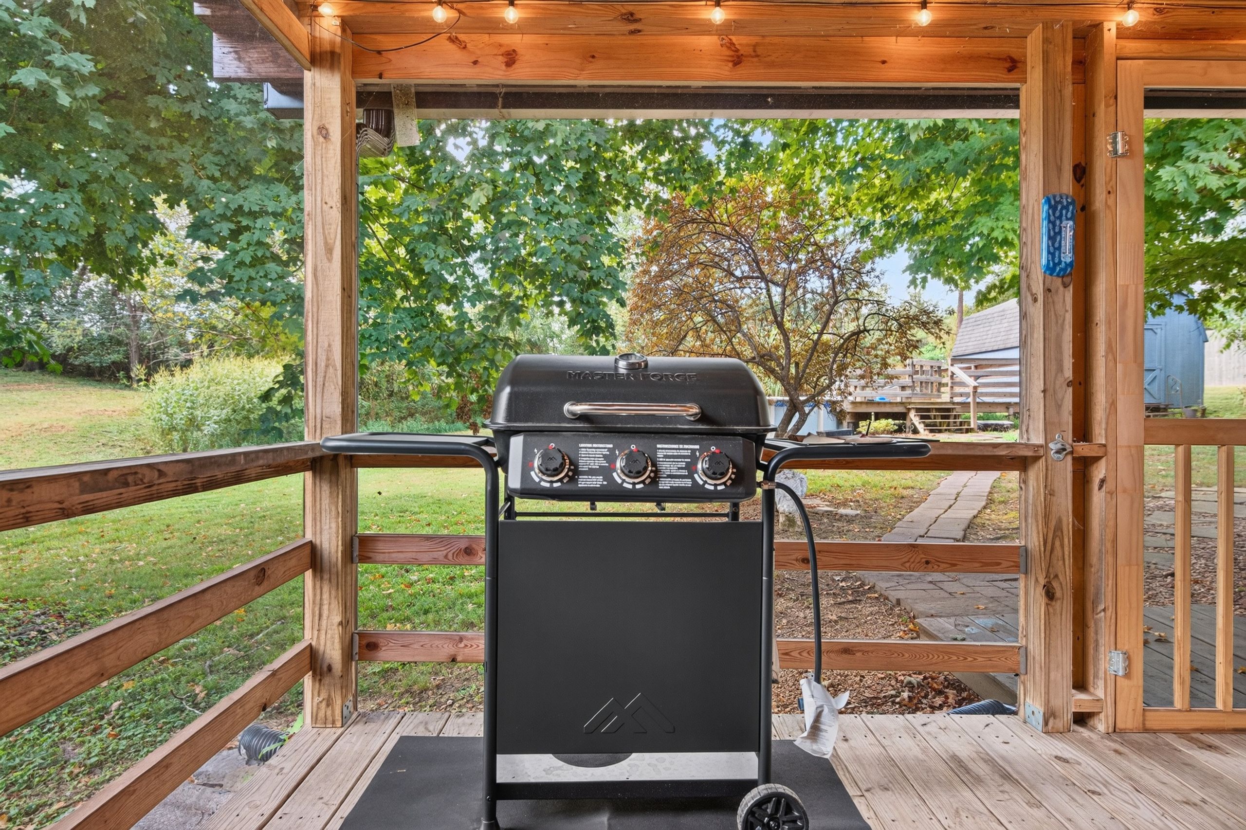 Un barbecue doté de commandes, installé sur une terrasse en bois, d’où l’on peut admirer un jardin et une clôture en bois.