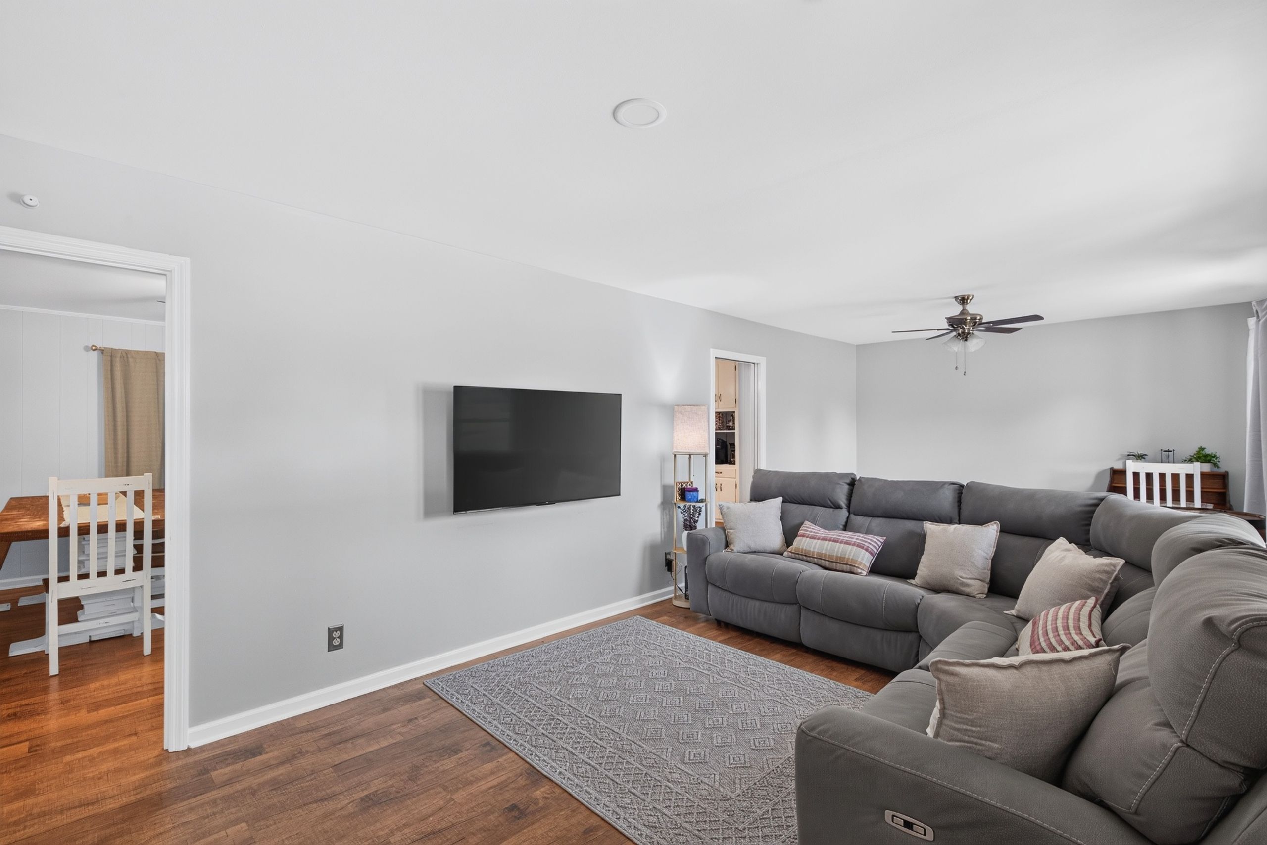 A modern living room with a grey sofa, a flat-screen TV, and a ceiling fan.
