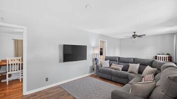 A modern living room with a grey sofa, a flat-screen TV, and a ceiling fan.