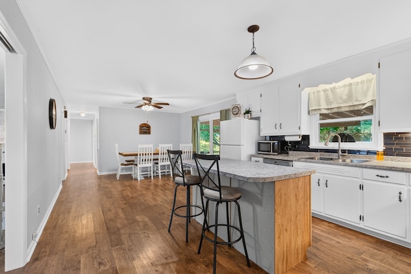 A modern kitchen with white cabinetry, a wooden island, and a dining area with white chairs.