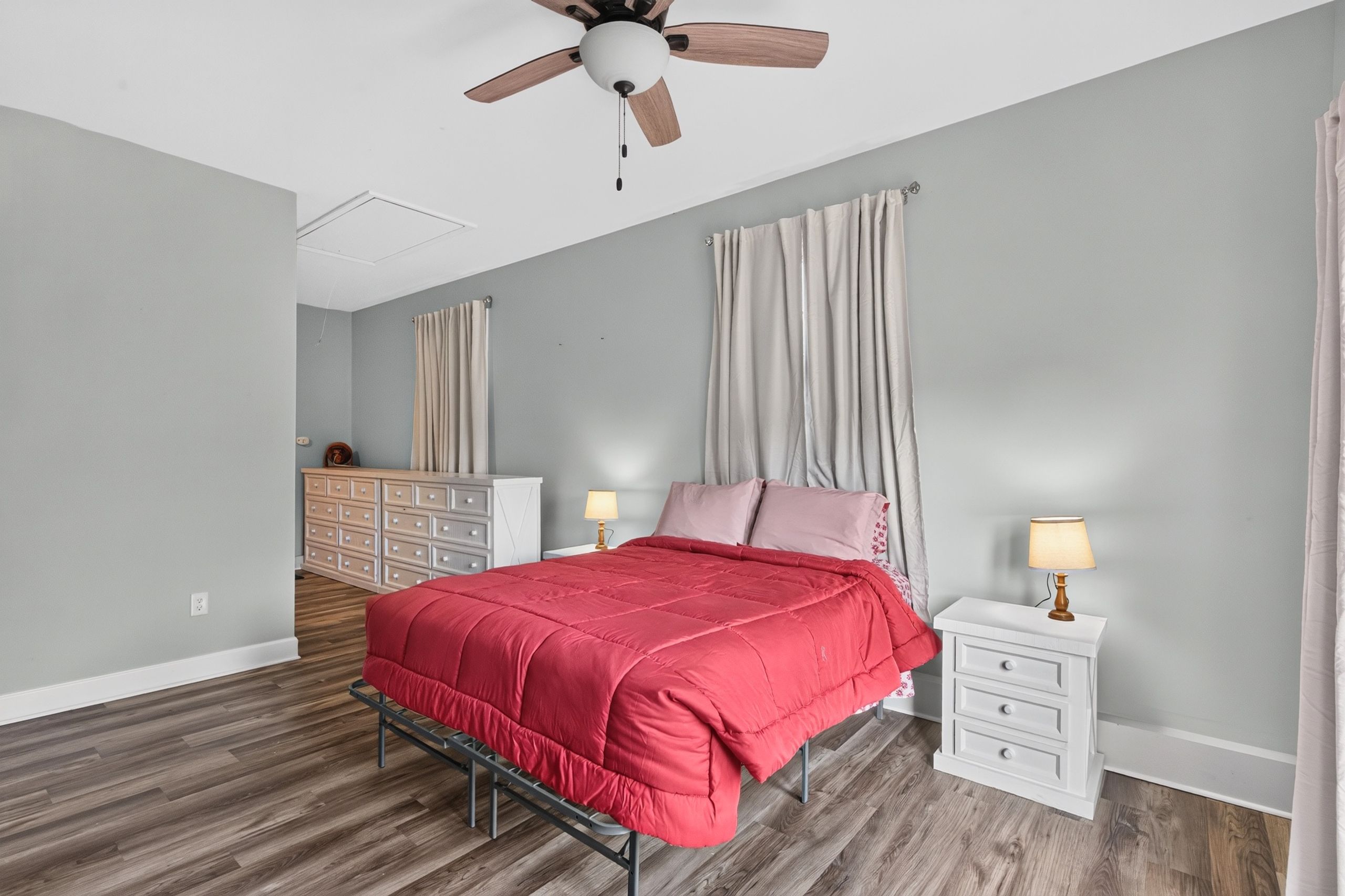 A bedroom with a bed, nightstands, a dresser, a ceiling fan, and a window with curtains.