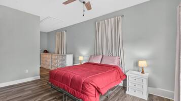 A bedroom with a bed, nightstands, a dresser, a ceiling fan, and a window with curtains.