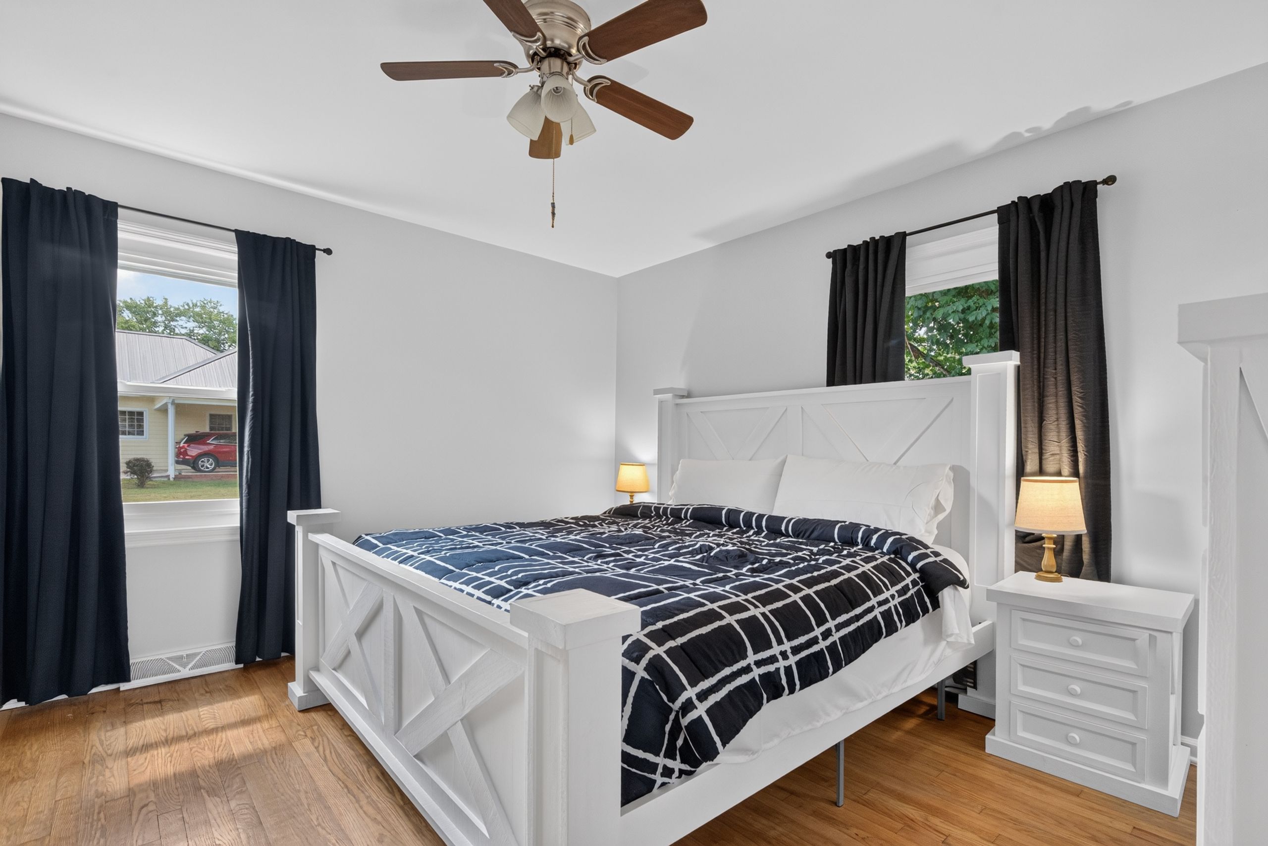Een slaapkamer met een bed, nachtkastjes, een plafondventilator en uitzicht op het omliggende landschap.
