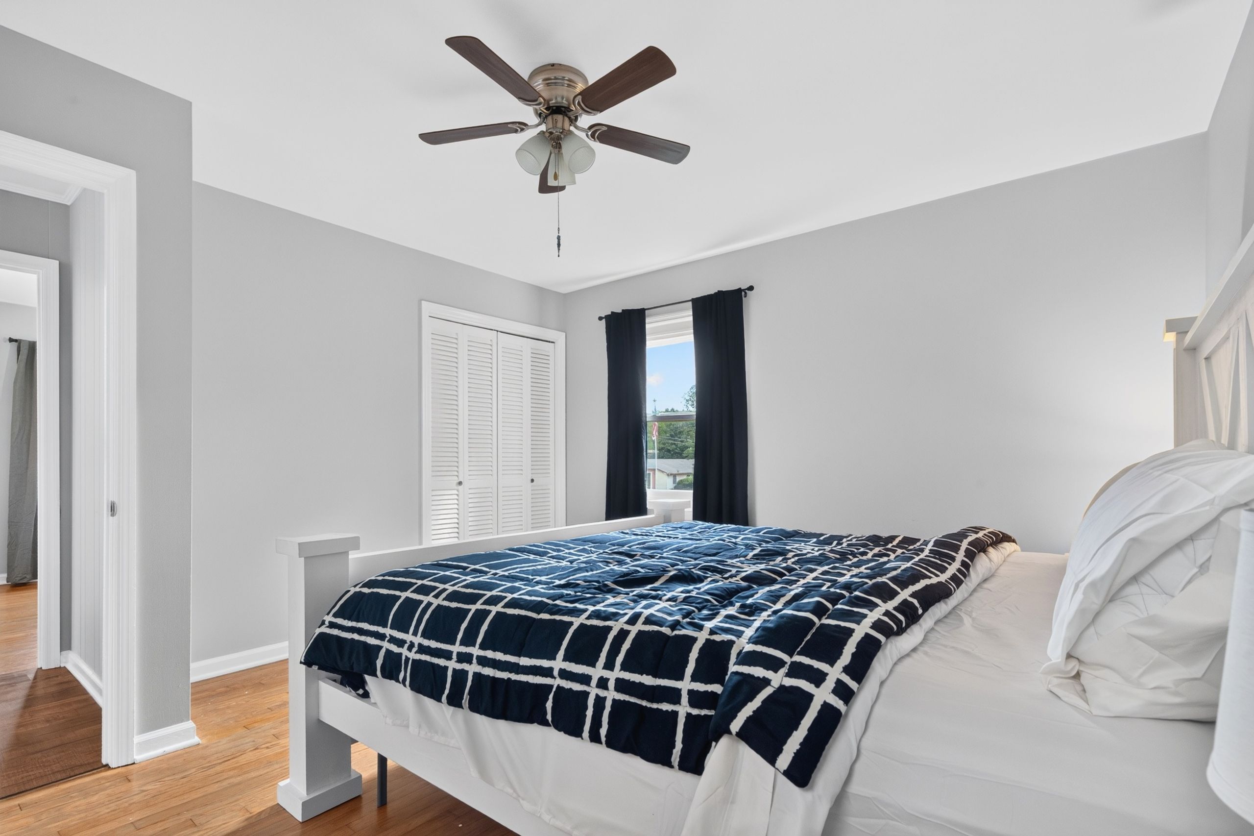 Un dormitorio con cama, ventilador de techo, ventana con cortinas y una puerta.