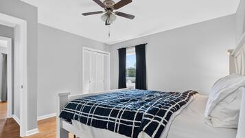 Un dormitorio con cama, ventilador de techo, ventana con cortinas y una puerta.