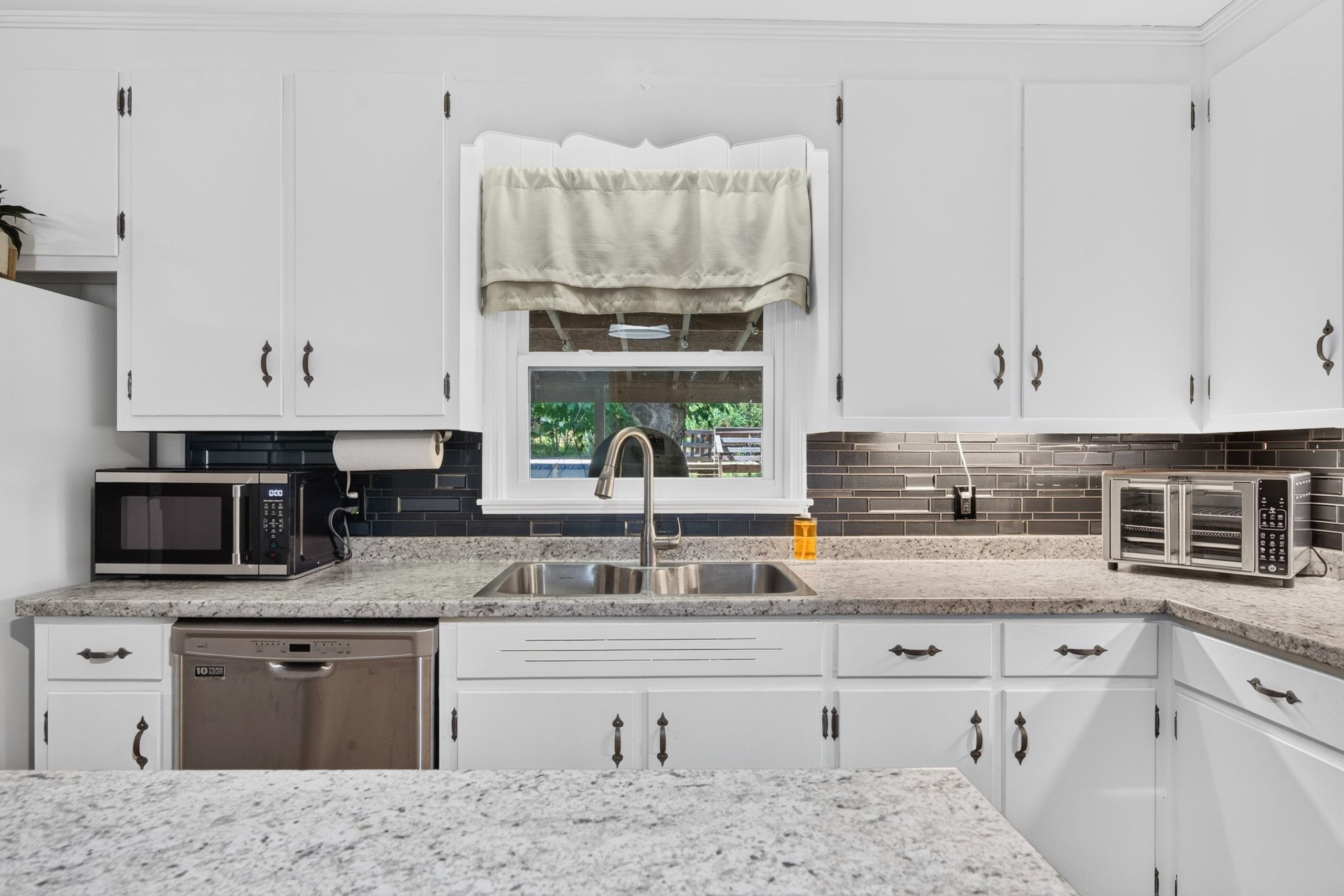 A modern kitchen with white cabinets, a stainless steel sink, a microwave, and a toaster.