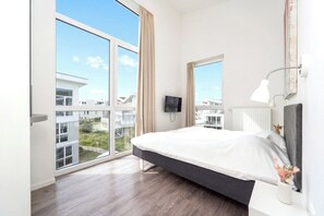 A modern hotel room with a large bed, a TV, and a view of the cityscape. - Dune Villa 02 Penthouse 05 (Lübeck-Travemünde)
