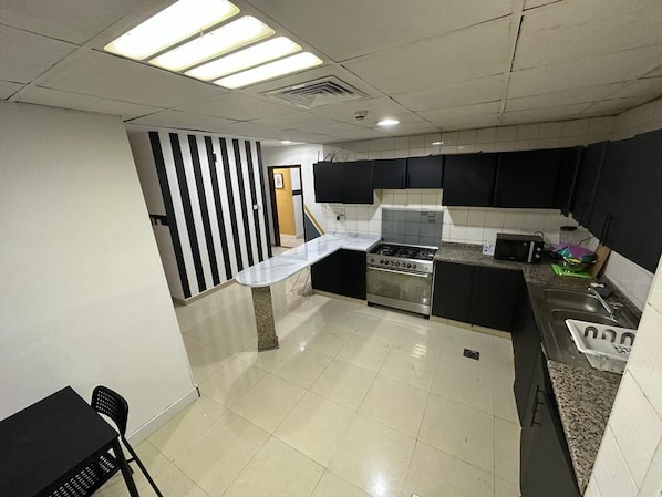 A kitchen with a stove, sink, and black cabinets. - Double Bed Partition Room in Al Barsha1 (Dubai)