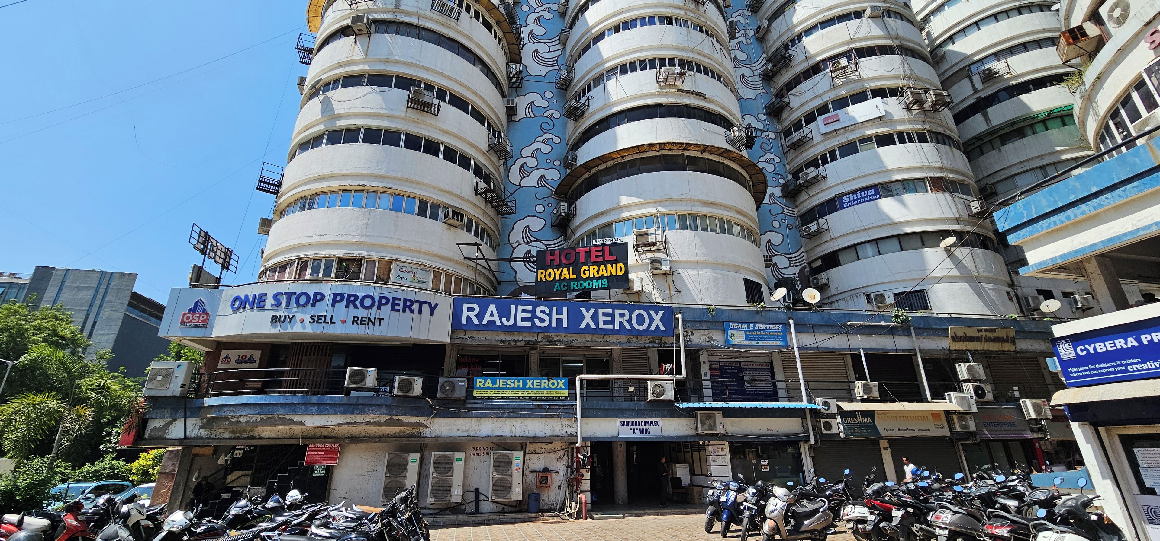 Un edificio de varios pisos con comercios en la planta baja, incluyendo una agencia inmobiliaria, una tienda de fotocopiado y un hotel.