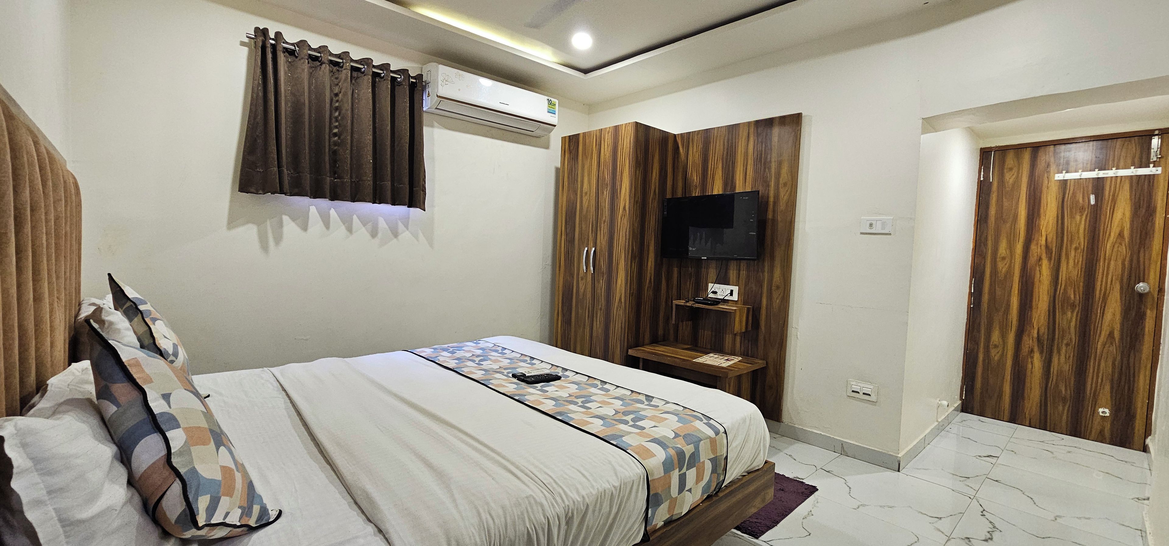 Un dormitorio con cama, televisor montado en una pared de madera, armario y una mesita con control remoto.