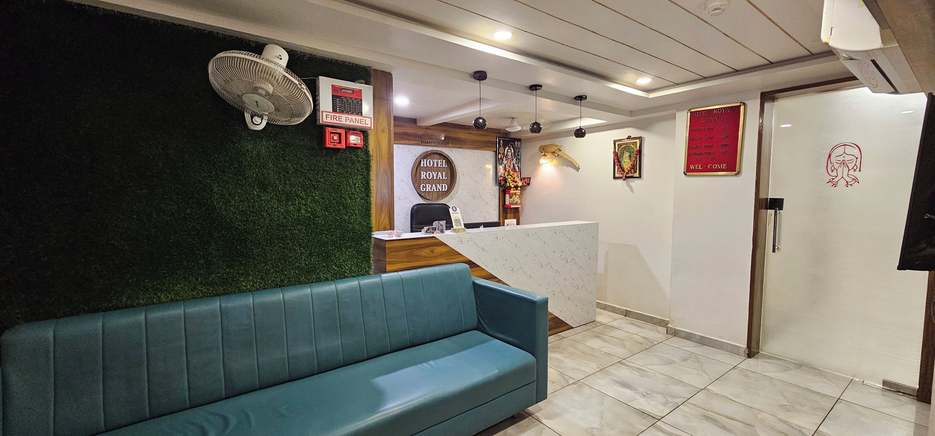 Zona de recepción de hotel con un sofá tapizado en verde, un mostrador de recepción y un cartel de panel contra incendios.