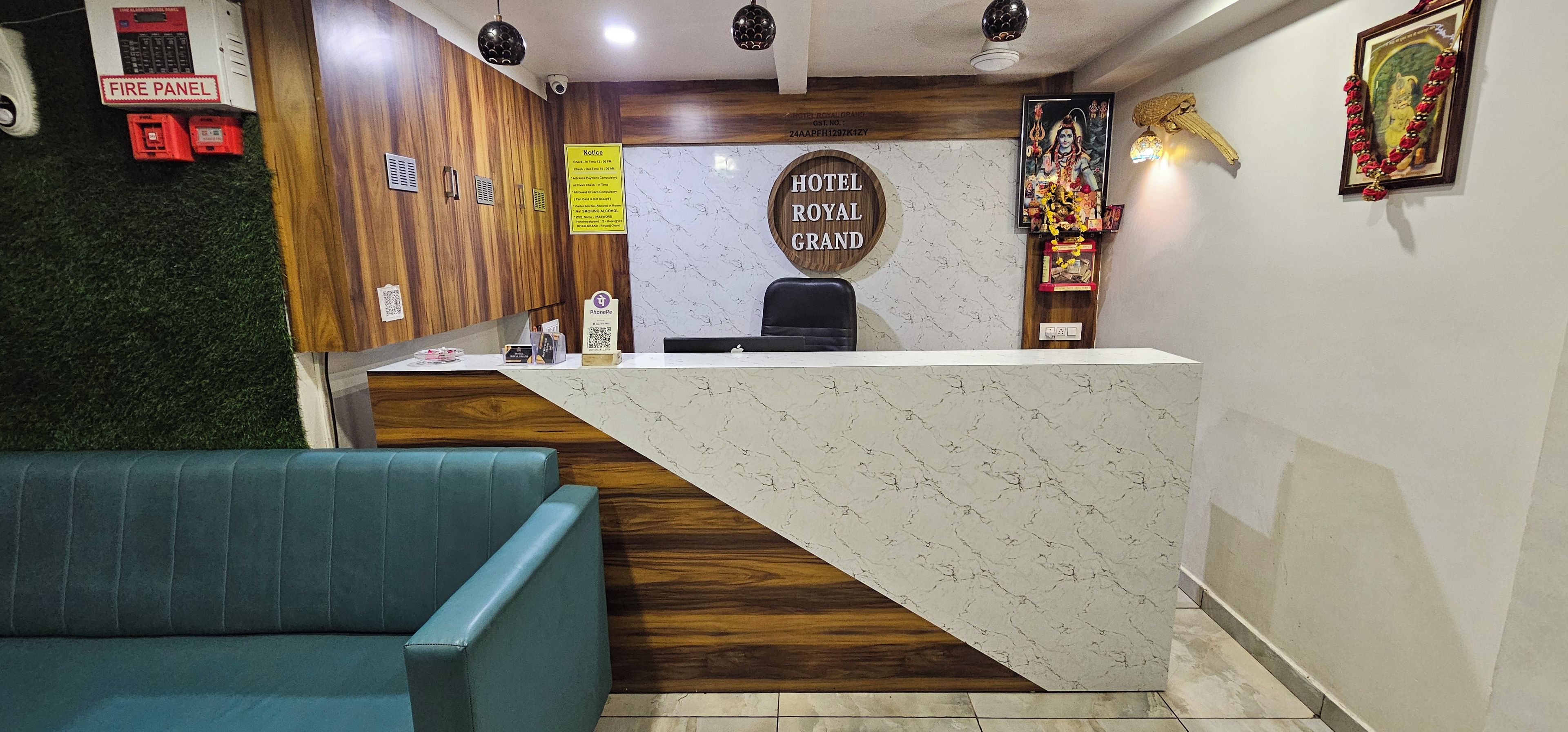 Zona de recepción de hotel con un mostrador de madera, un sofá azul y un letrero en la pared que dice 'HOTEL ROYAL GRAND'.