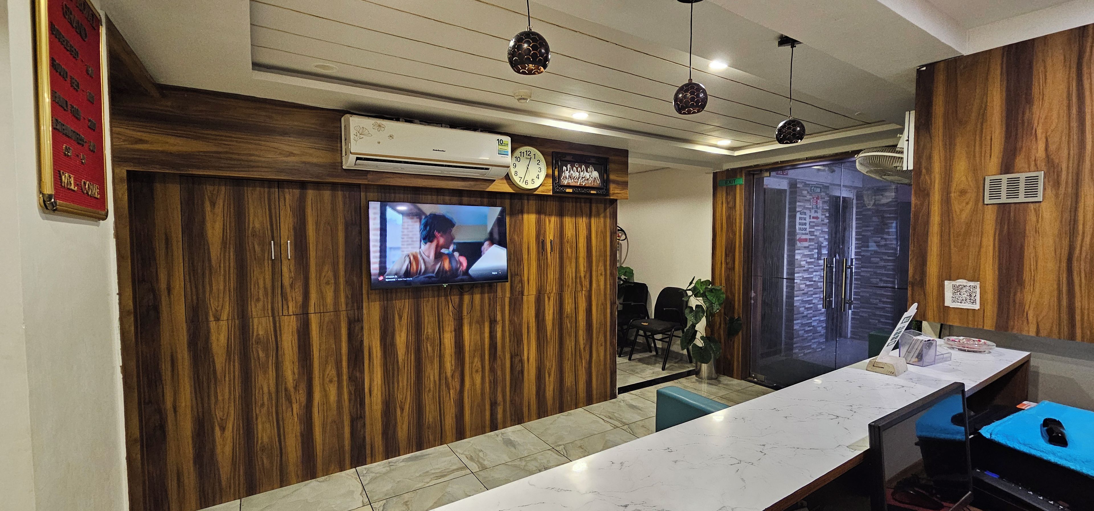 Un área de recepción con un mostrador de madera, un televisor montado y una unidad de aire acondicionado mural.