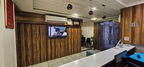 Ett entréområde med en receptionsdisk i trä, en väggmonterad tv och en väggmonterad luftkonditioneringsanläggning.