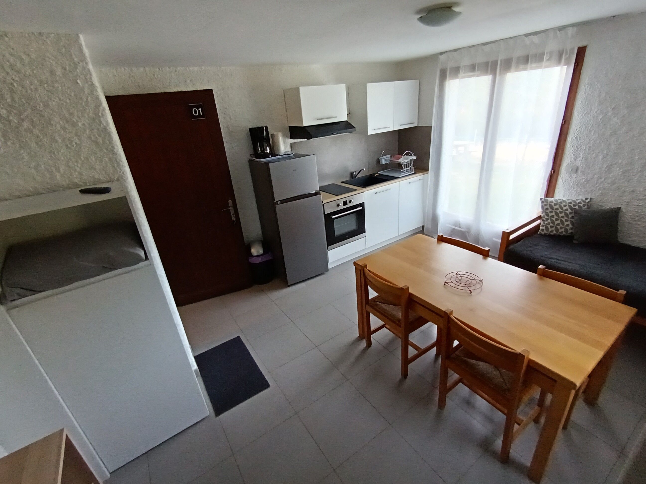 Eine kleine Küche mit Kühlschrank, Herd und Mikrowelle. Es gibt einen Esstisch mit Stühlen und eine Couch mit Kissen.